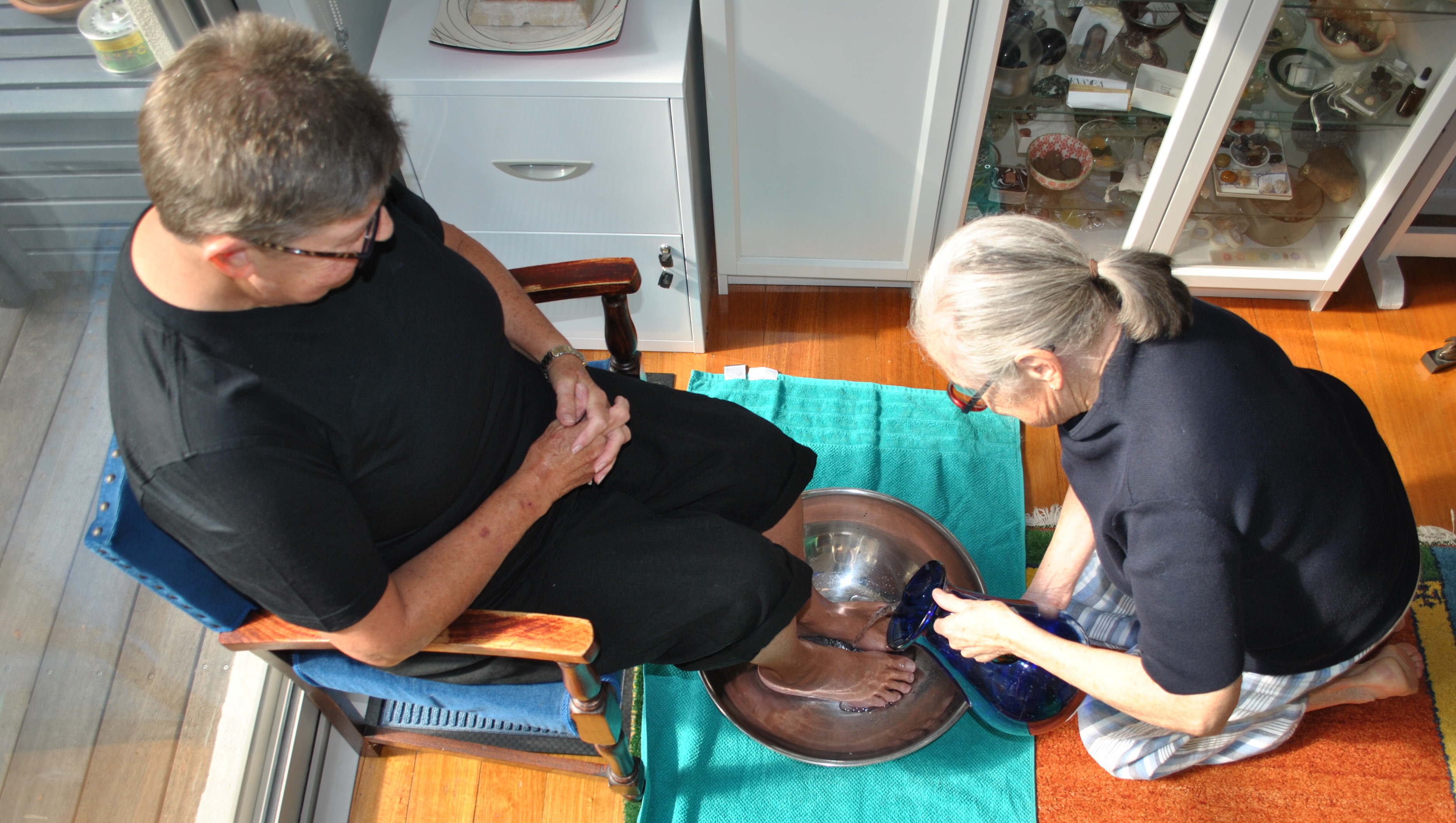 Nonie kneeling, pouring water on a client's feet